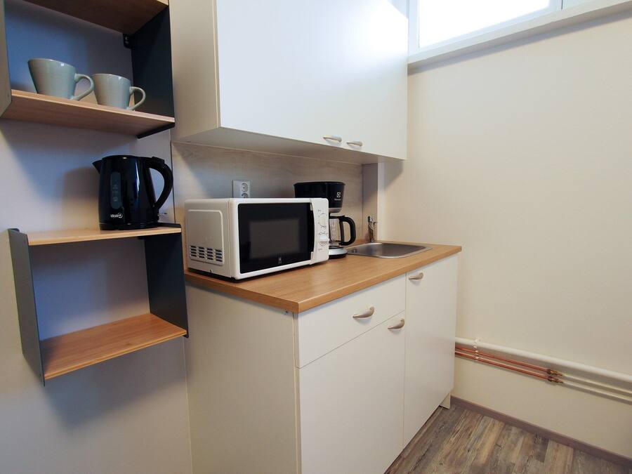 Una kitchenette compacta con microondas, cafetera y un estante con tazas.