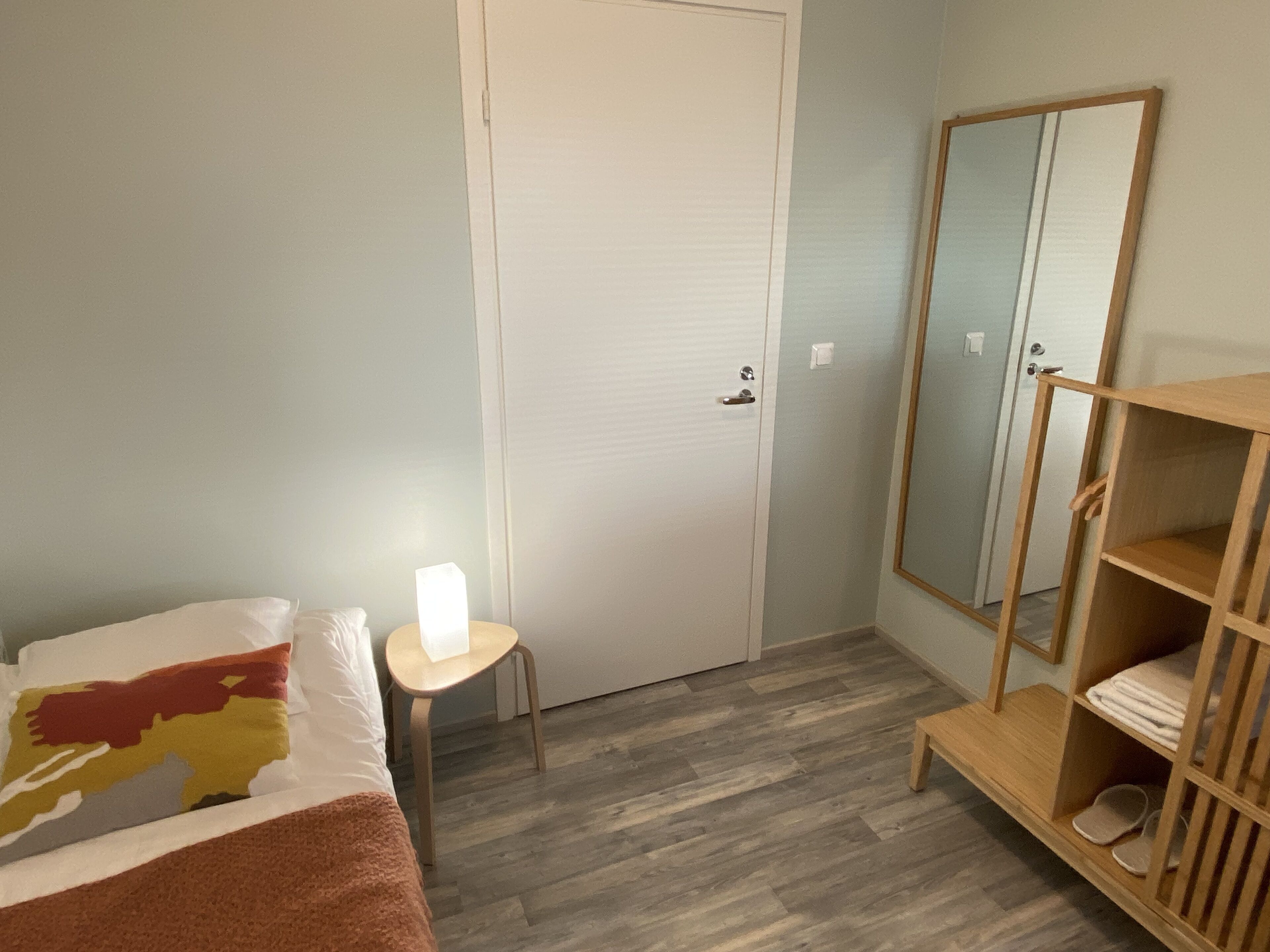 Ein Schlafzimmer mit einem Bett, einem kleinen Tisch mit Lampe, einem Kleiderschrank und einem Spiegel.
