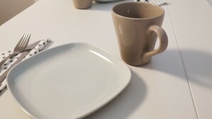 A dining area with a white table set for two, including plates, a mug, and cutlery. A microwave, coffee maker, and a kettle are visible on the counter. - Savonlinna Rentals (Savonlinna)
