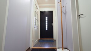 A narrow hallway with a black door at the end, a wooden coat rack, and a blue mat at the entrance. - Savonlinna Rentals (Savonlinna)