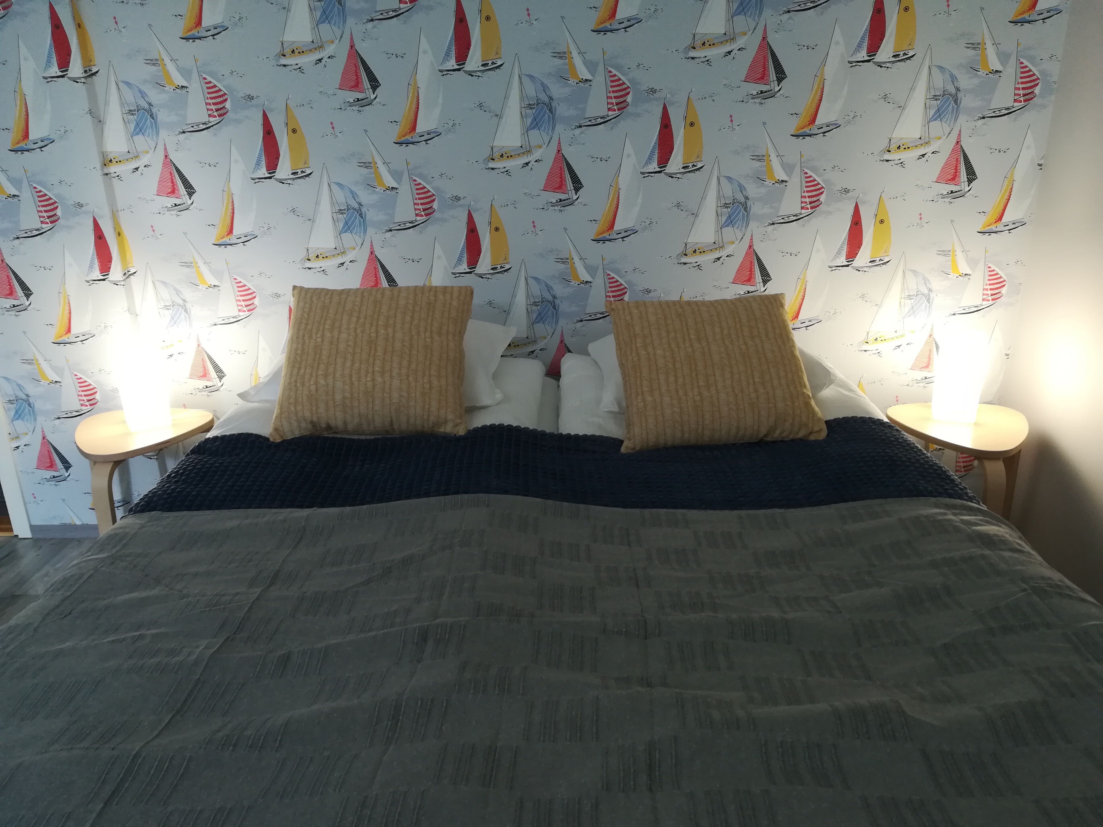 A bedroom with a bed, two pillows, two bedside tables, and a wall with a sailboat pattern.