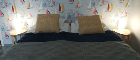 A bedroom with a bed, two pillows, two bedside tables, and a wall with a sailboat pattern.