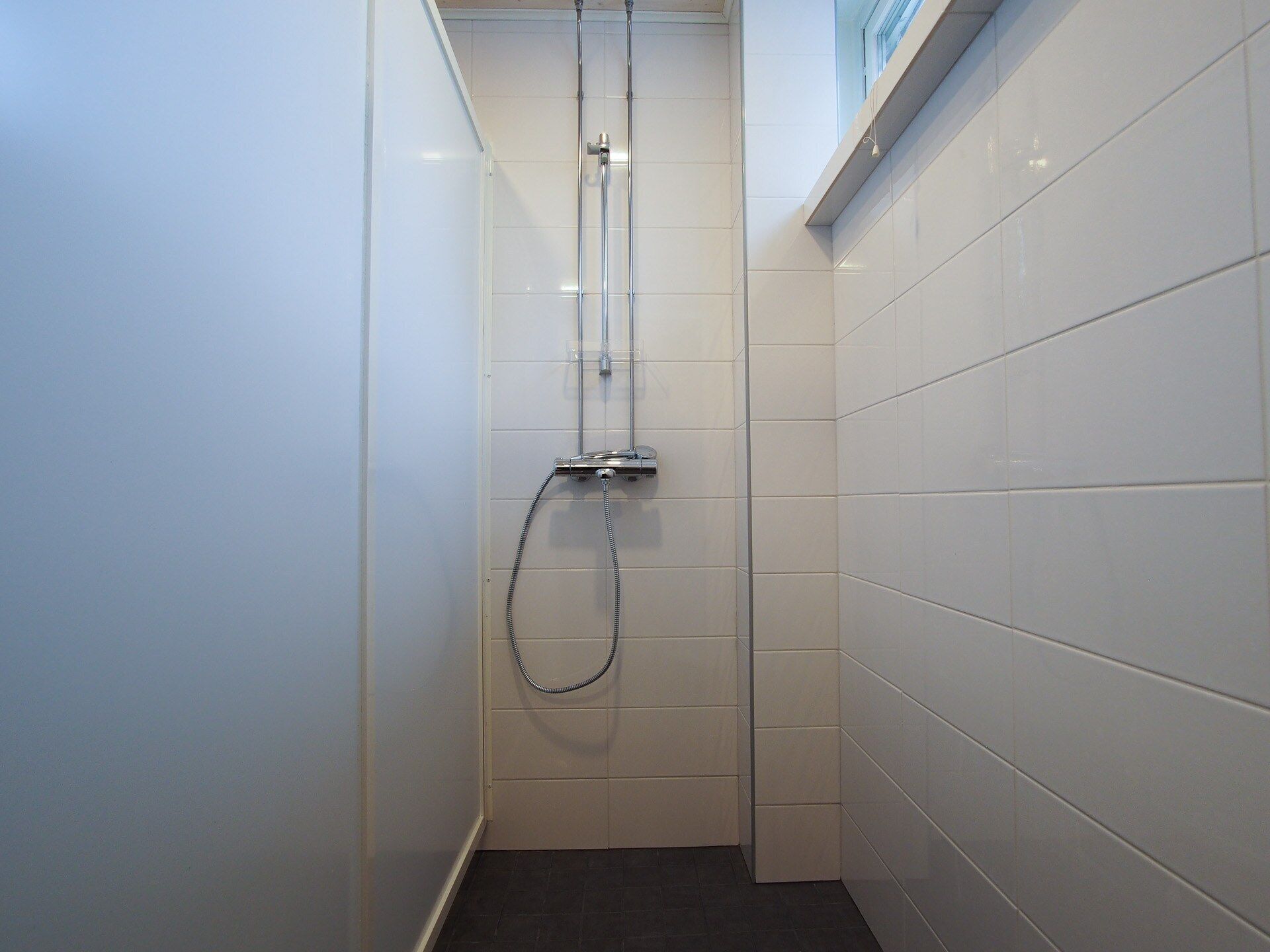 Un baño pequeño y estrecho con paredes de azulejos blancos y suelo oscuro.
