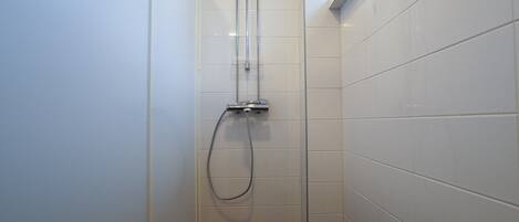 Un baño pequeño y estrecho con paredes de azulejos blancos y suelo oscuro.