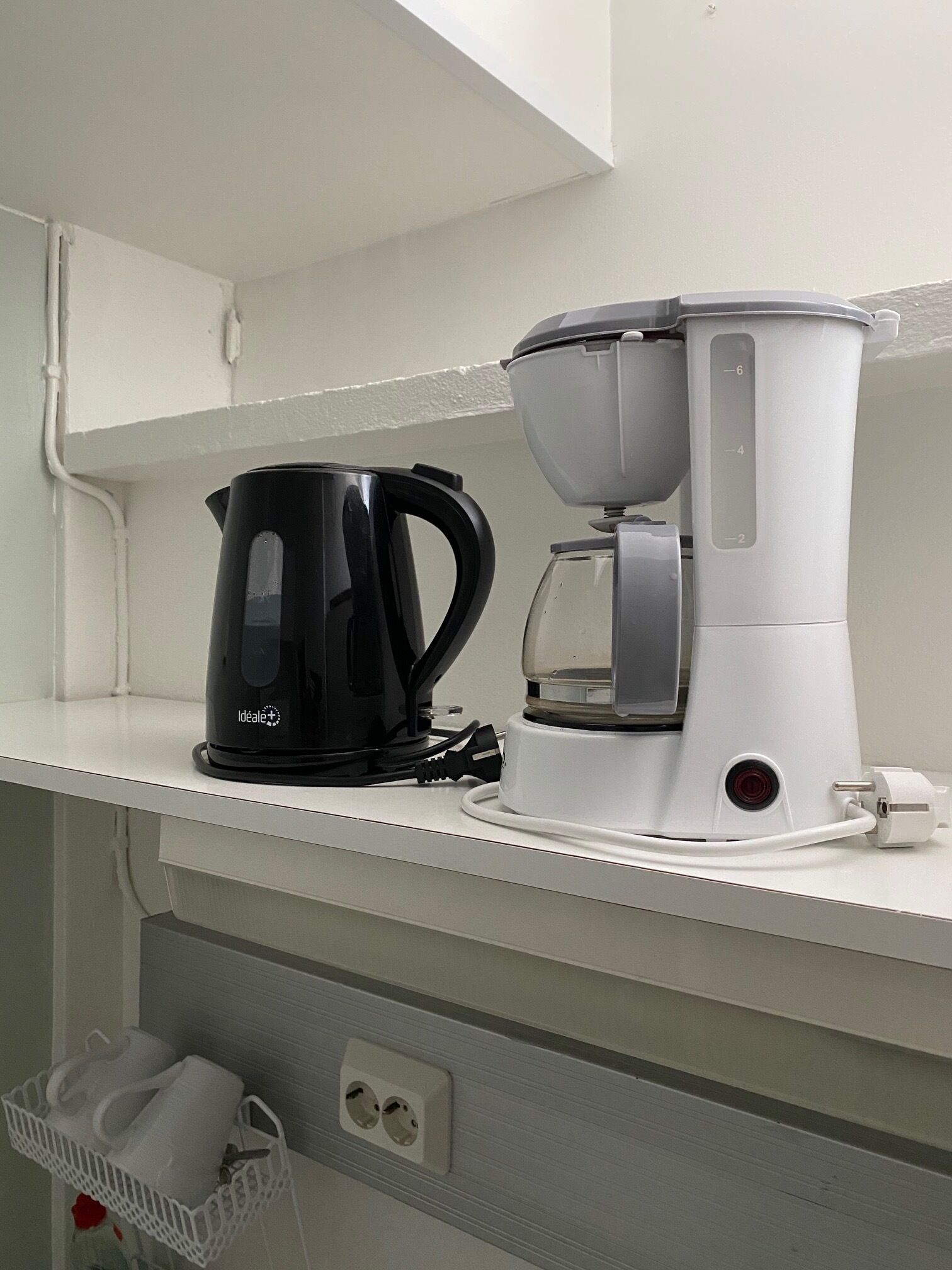 Una kitchenette con cafetera, hervidor y una encimera blanca.
