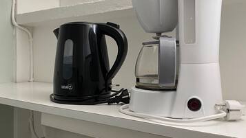 Una kitchenette con cafetera, hervidor y una encimera blanca.