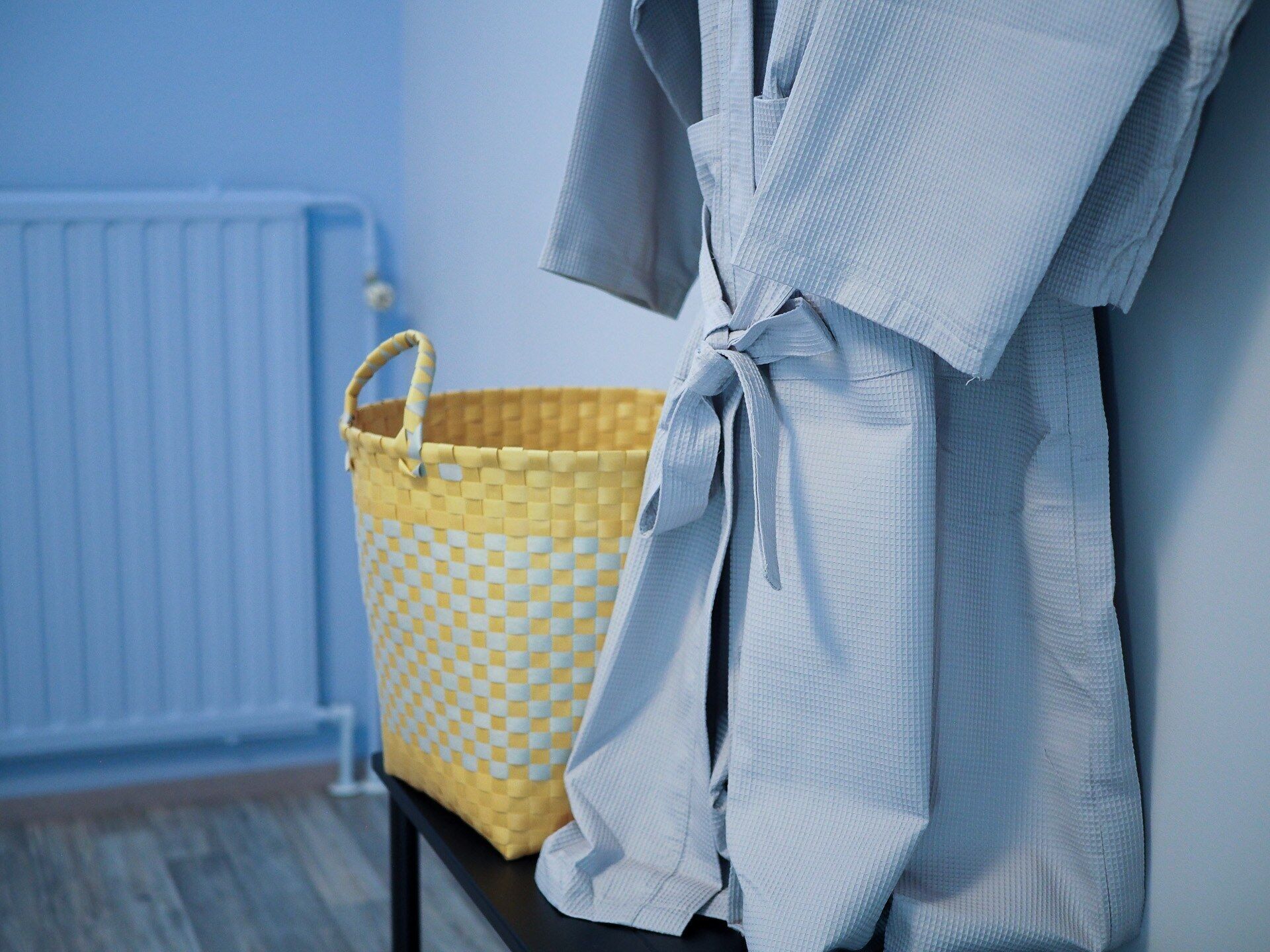 Un baño con una bañera blanca, una cesta amarilla de cuadros y una pared azul.