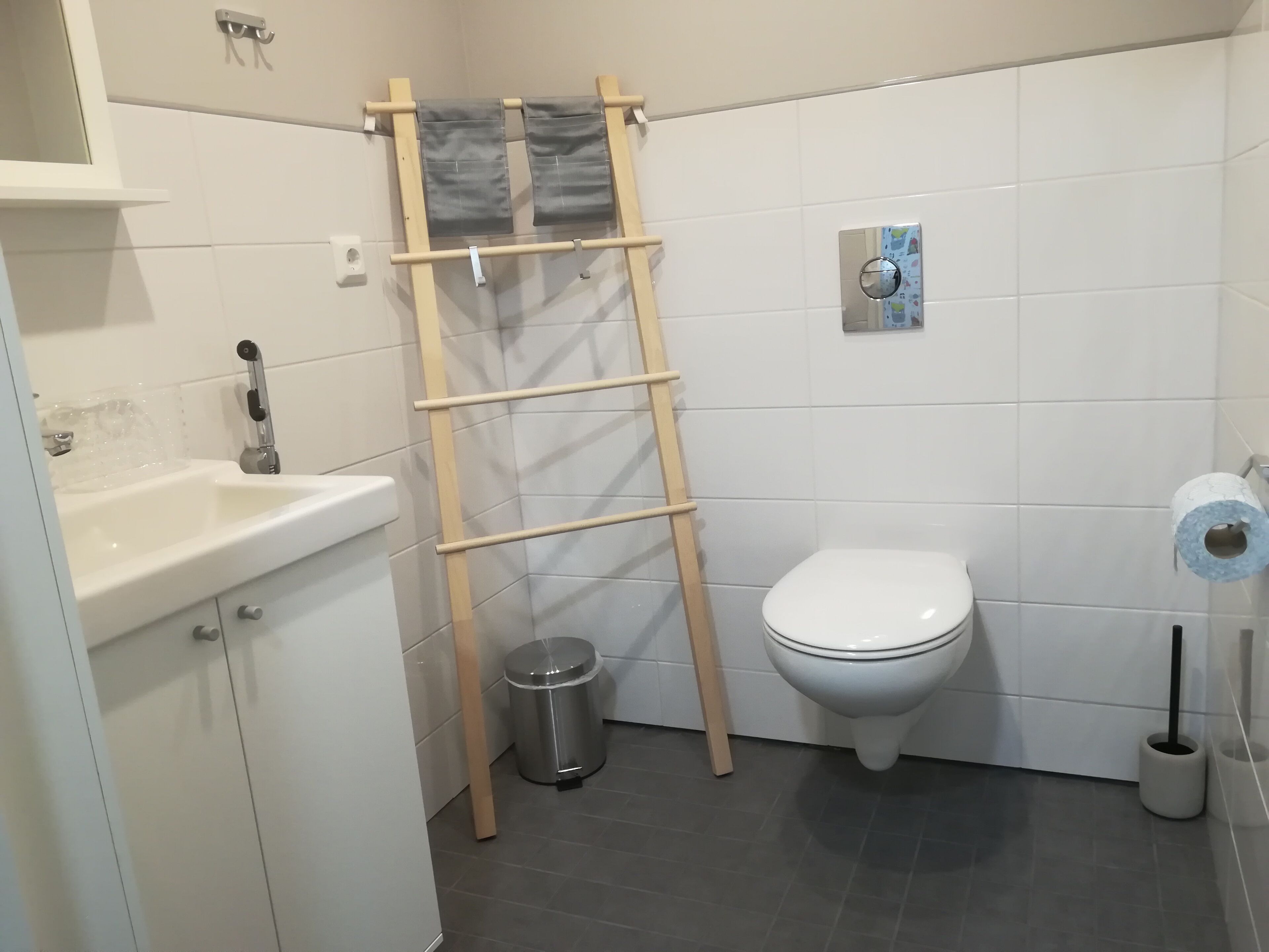 Un baño con un lavamanos blanco, inodoro y una escalera de madera apoyada en la pared.