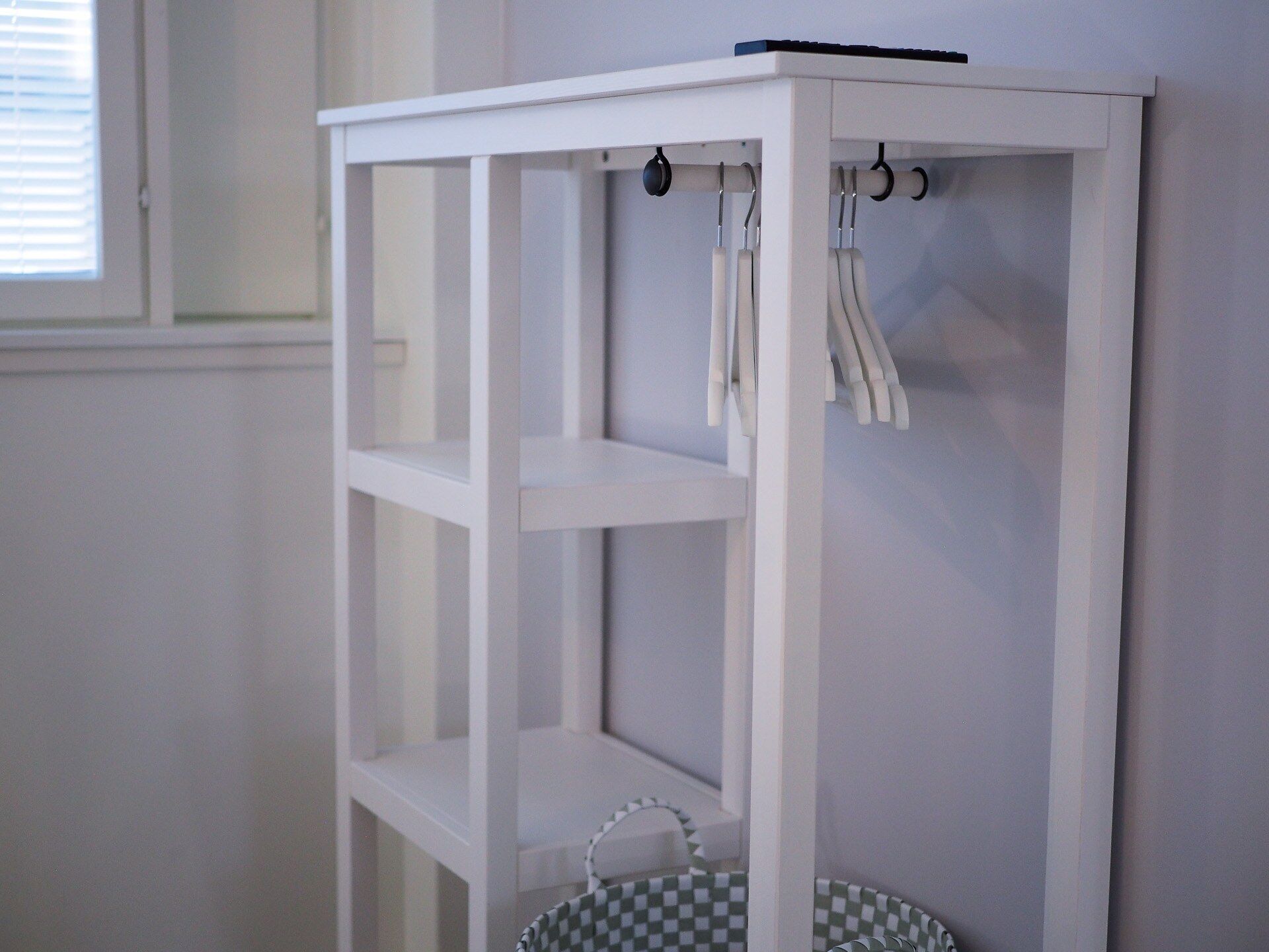 A white, three-tiered, open shelving unit with hooks on top.