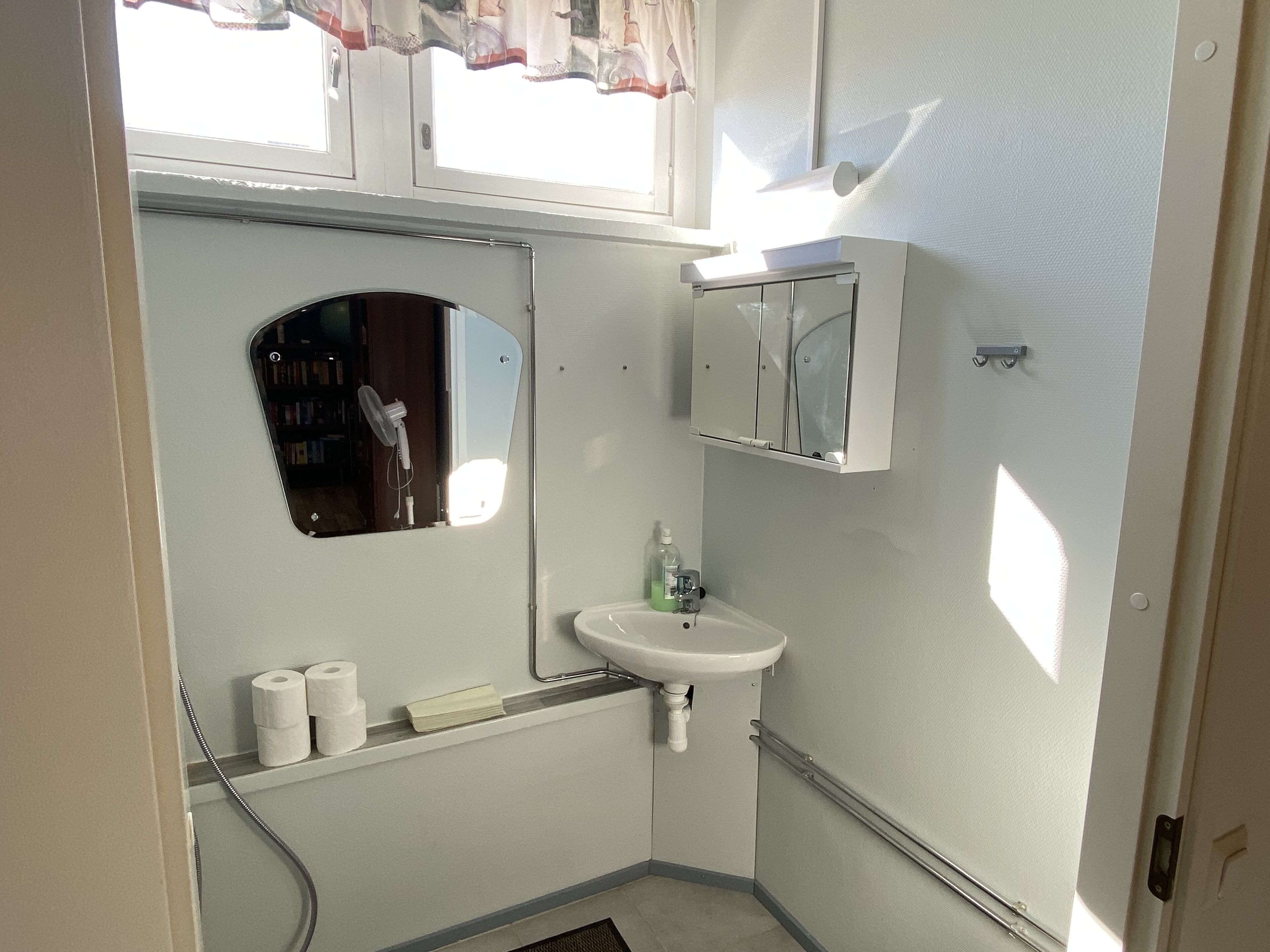 Un baño pequeño con un lavabo blanco, un espejo y una ventana con cortinas.