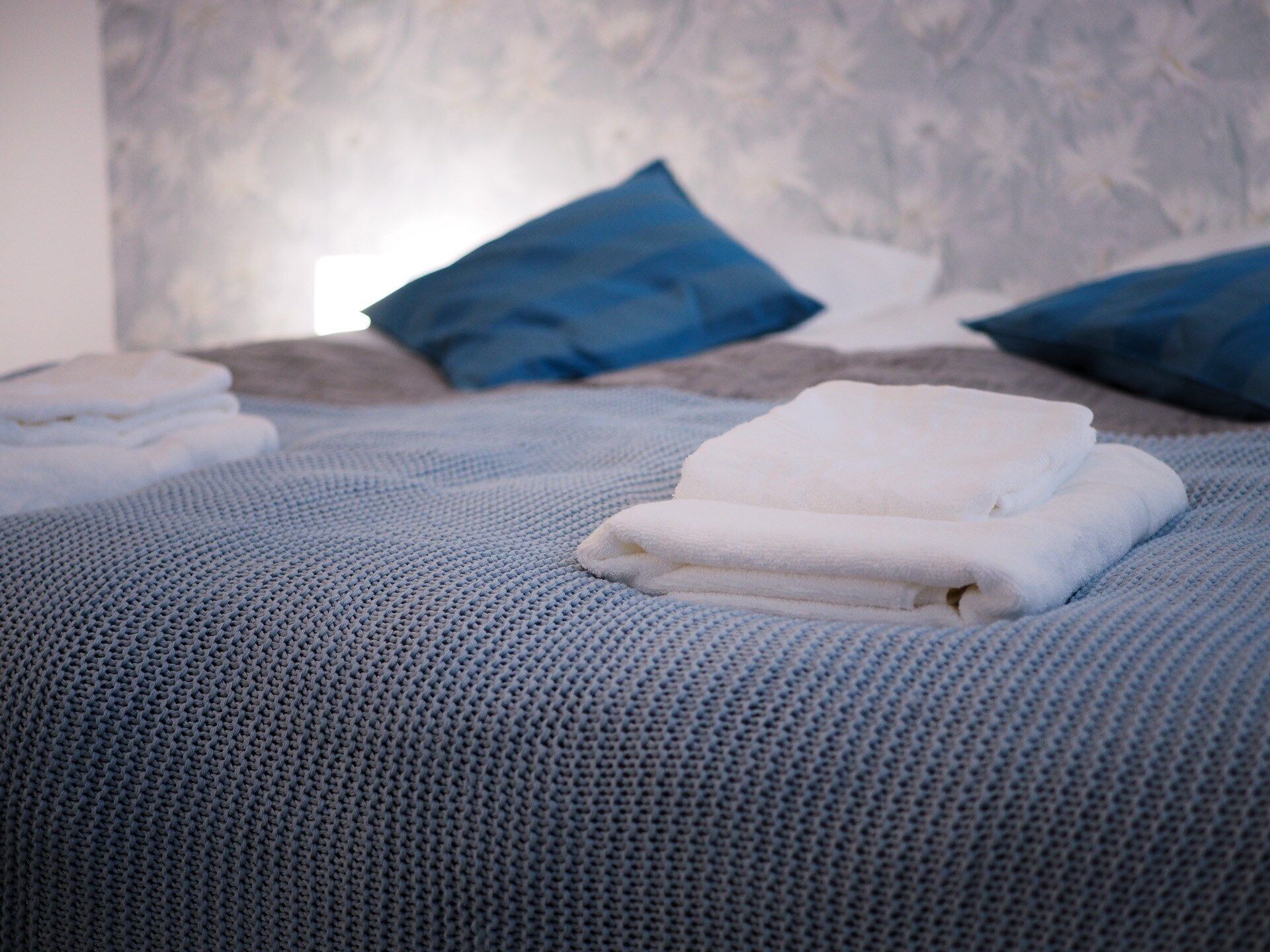 Un lit bien fait, avec une literie bleue et des serviettes blanches, deux oreillers bleus et un mur à motifs en arrière-plan.