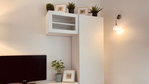 Ett modernt vardagsrum med en platt-TV, en vit TV-möbel, ett litet bord och en väggmonterad lampa.