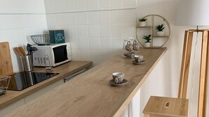 Ett kök med en bänkskiva i trä, en mikrovågsugn, ett litet handfat och en pall i trä.
