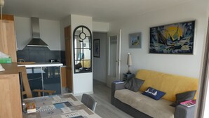 Ett kompakt bostadsutrymme med ett litet kök, en matplats och en soffa med kuddar.
