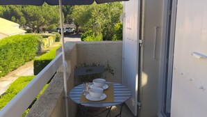 A small balcony with a table and chairs, a blue umbrella, and a view of the surrounding greenery.