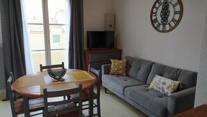 A living room with a sofa, a table with chairs, a television on a stand, and a wall clock.
