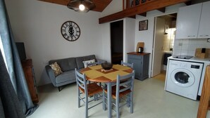 A compact living space with a dining area, a sofa, a washing machine, and a kitchen.
