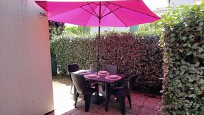 Une terrasse extérieure avec une table et des chaises, un parasol rose et une haie en arrière-plan.