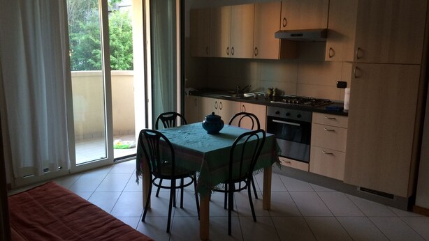 Een kleine keuken met een eettafel, stoelen, een fornuis en keukenkastjes.