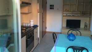 Een kleine keuken met een gasfornuis, oven en een eethoek met een tafel en stoelen.