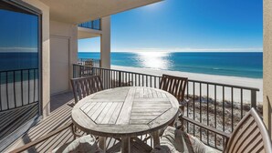 A wooden table and chairs on a balcony with a view of the ocean.