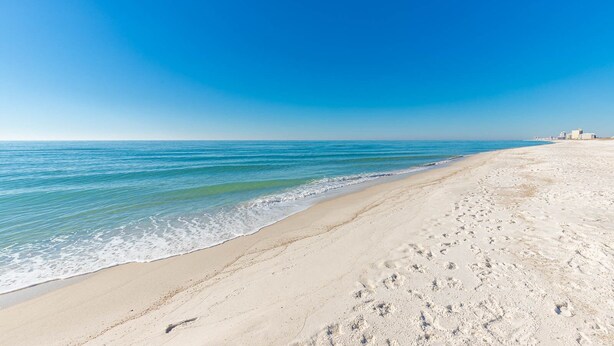 A beach with a clear sky, calm sea, and footprints in the sand.