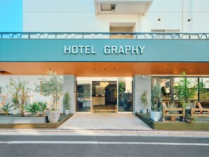 A hotel entrance with a sign reading 'HOTEL GRAPHY,' large windows, and potted plants.