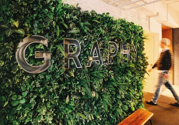 A wall with the word 'GRAPHY' in large letters, surrounded by dense green foliage.