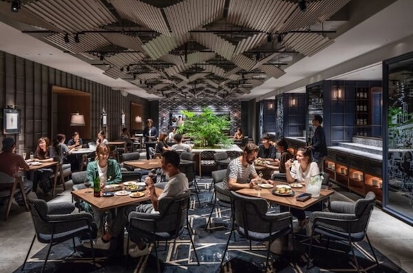 A modern restaurant with a central dining area, individual tables, and a bar area with seating.