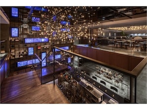 Eine moderne Bar mit mehreren Bildschirmen, einer Treppe und Sitzgelegenheiten.