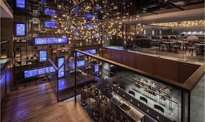 Eine moderne Bar mit mehreren Bildschirmen, einer Treppe und Sitzgelegenheiten.