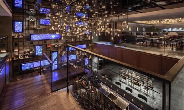 A modern bar area with multiple screens, a staircase, and seating.