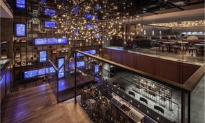 Un bar moderno con varias pantallas, una escalera y asientos.