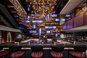 A modern bar area with multiple screens, a central bar, and seating.