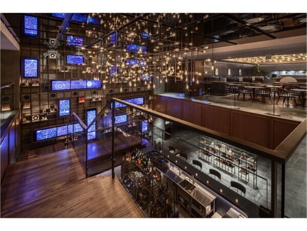 A modern bar area with multiple screens, a staircase, and seating.