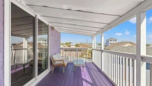 En overdækket balkon med gulv i lilla nuance, en glasdør, en fletstol og et lille bord.