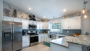 A modern kitchen with stainless steel appliances, white cabinetry, and a large island. - Best Family Vacation at the Beach or the Pool. (Tarpon Springs)