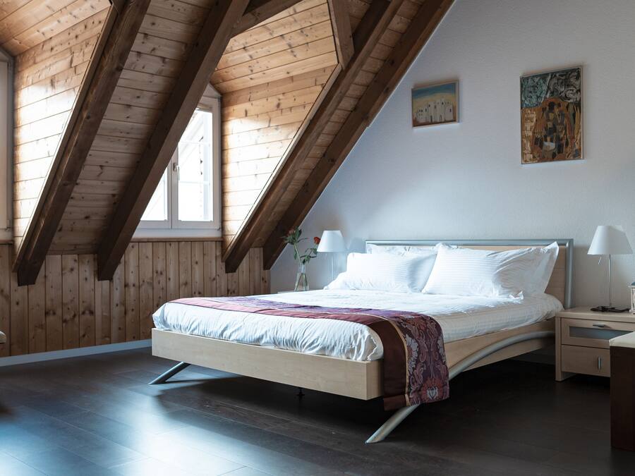 A bedroom with a wooden ceiling, a bed, a nightstand, and a window.