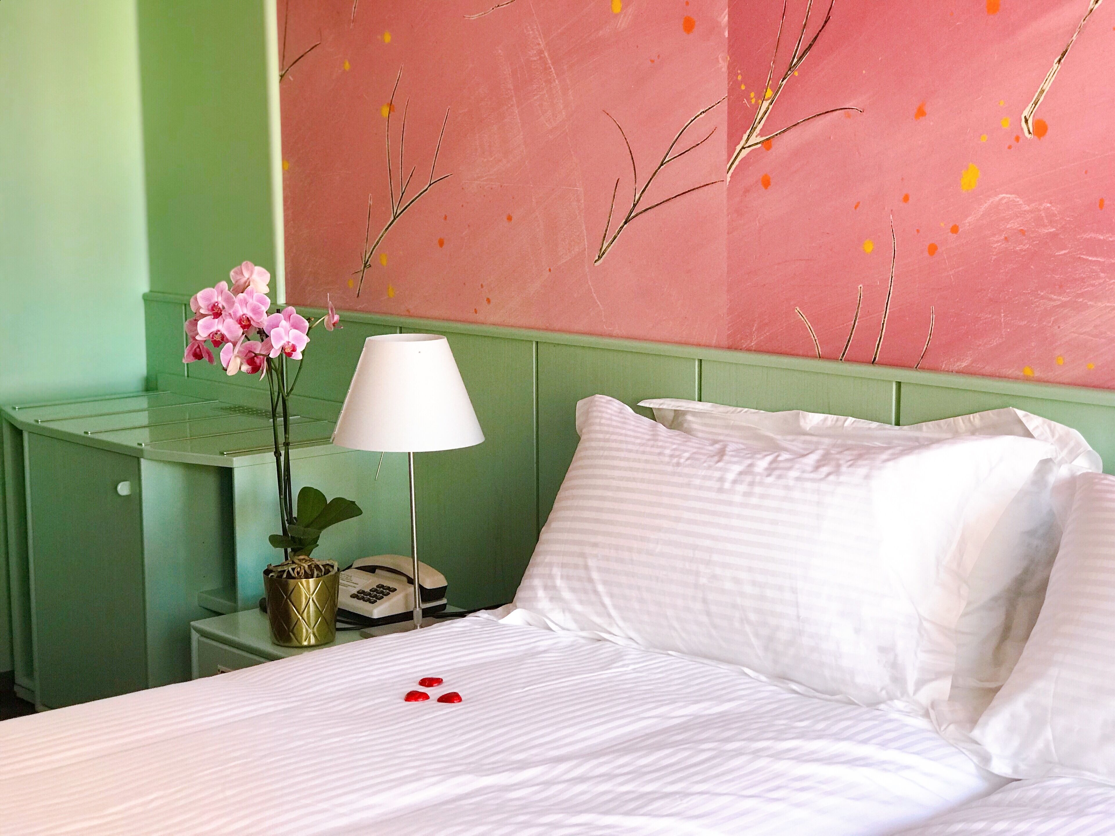 Une chambre d’hôtel avec un lit, une table de chevet avec une lampe, un vase avec des fleurs et un téléphone.