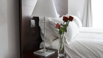 A hotel room with a bed, a bedside table with a lamp, and a vase with flowers.
