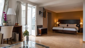 A hotel room with a bed, bedside tables, a desk, a chair, a TV, and a window with curtains. - Swiss Hotel La Couronne (Avenches)