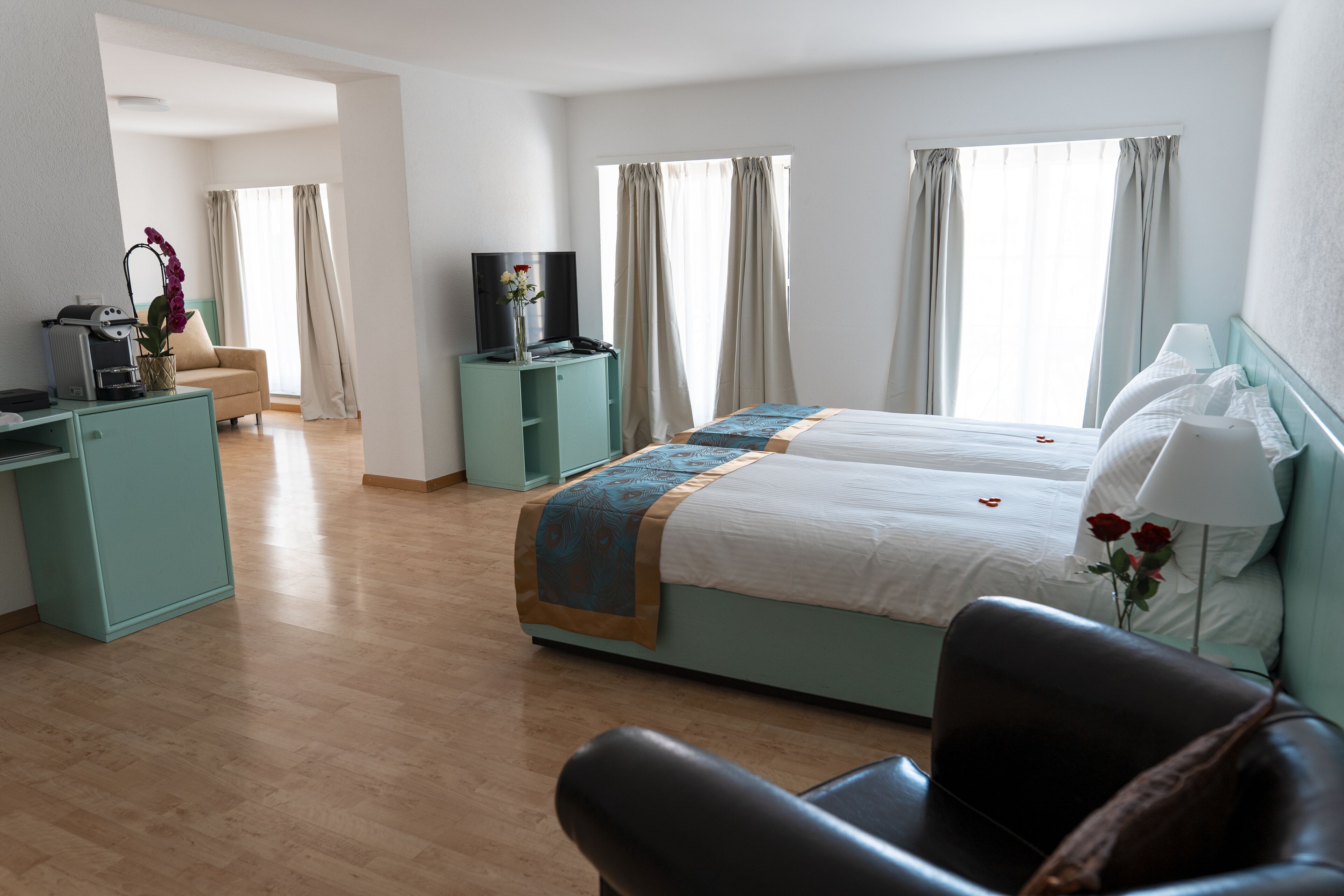 Una habitación de hotel con cama, escritorio, silla, televisor y ventana con cortinas.