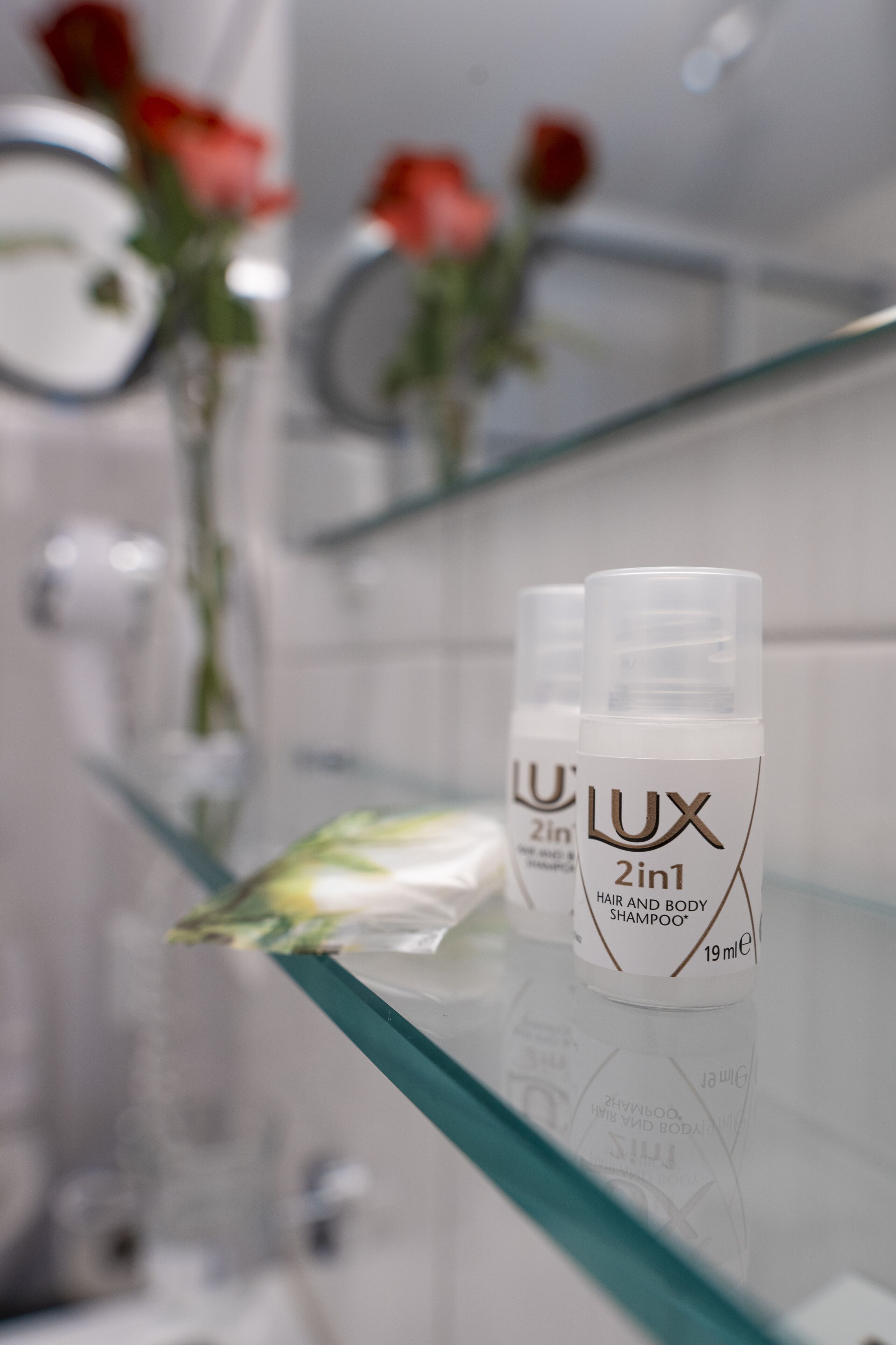 Two bottles of LUX 2in1 hair and body shampoo on a glass shelf in a bathroom.