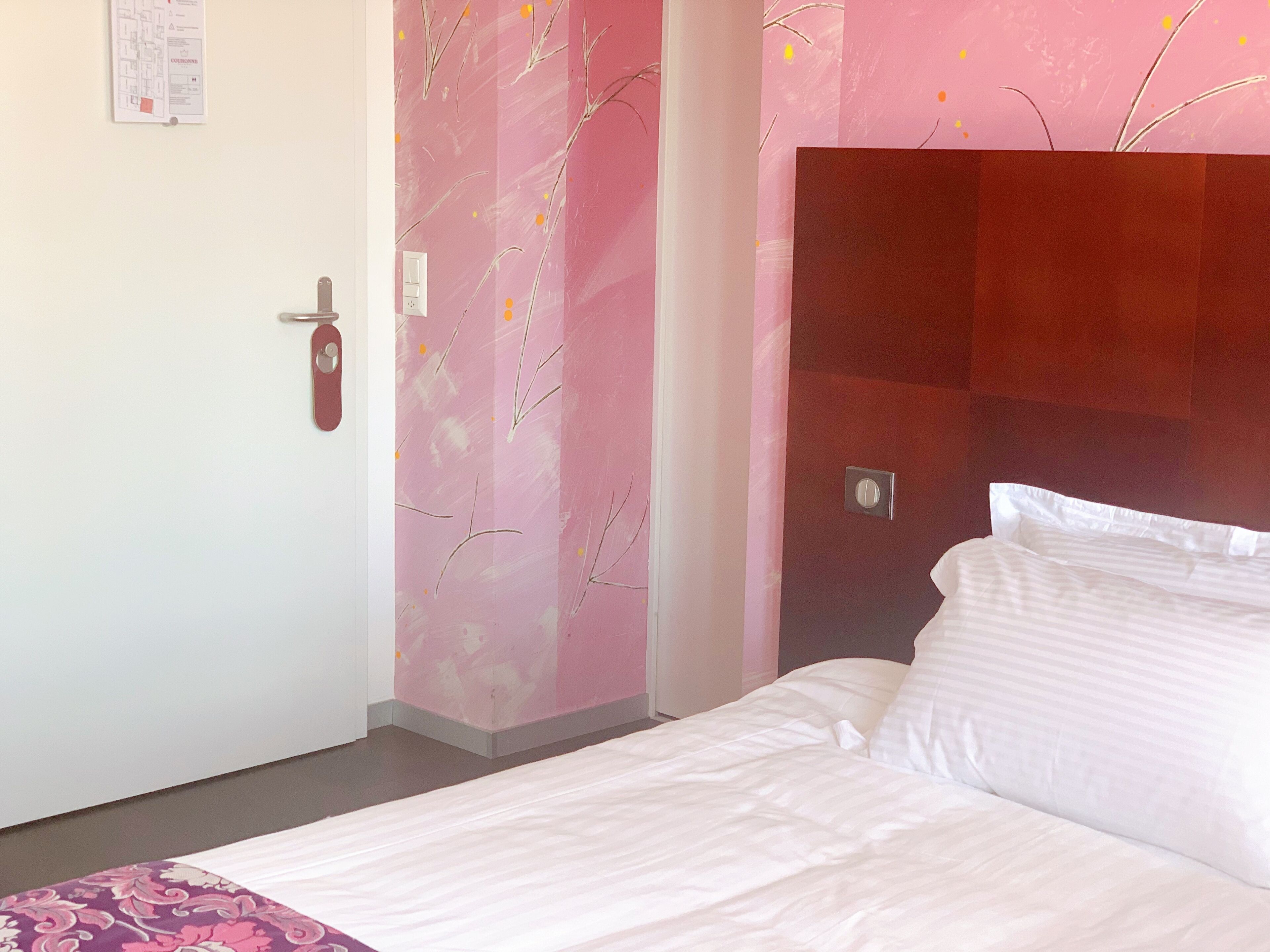 A hotel room with a bed, a door, and a wall with a pink floral pattern.