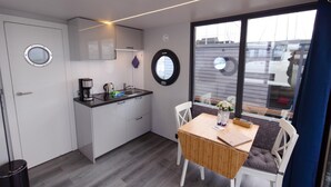 A compact kitchen with a sink, coffee maker, and cabinets. There's a dining table with chairs and a window with blinds. - Houseboat Fjord Aquila with roof terrace in Wendtorf (Wendtorf)