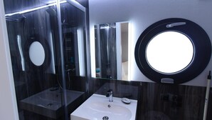 A modern bathroom with a round mirror, a white sink, and a glass-enclosed shower area. - Houseboat Fjord Aquila with roof terrace in Wendtorf (Wendtorf)