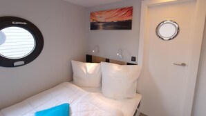 A bedroom with a bed, a round window, a door, and a painting on the wall. - Houseboat Fjord Aquila with roof terrace in Wendtorf (Wendtorf)