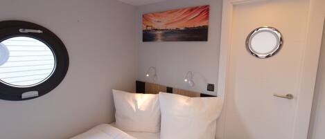 A bedroom with a bed, a round window, a door, and a painting on the wall.