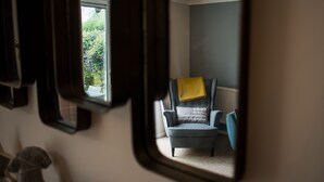 Una habitación con ventana, una silla con un cojín amarillo y una estatua.