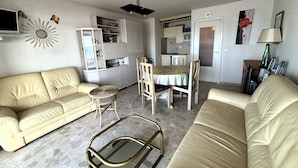 Un espacio habitable compacto con un sofá, una mesa de comedor con sillas, una pequeña cocina y un espejo decorativo en la pared.